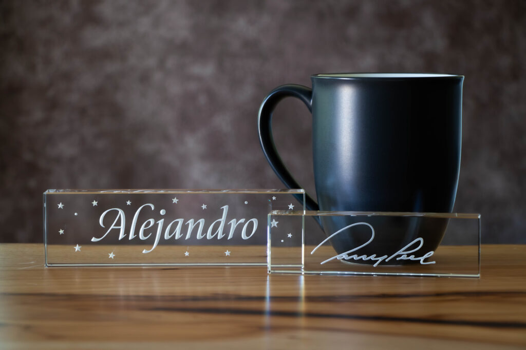 Two different sizes of sandcarved rectangular crystal name plates next to a coffee cup for size comparison